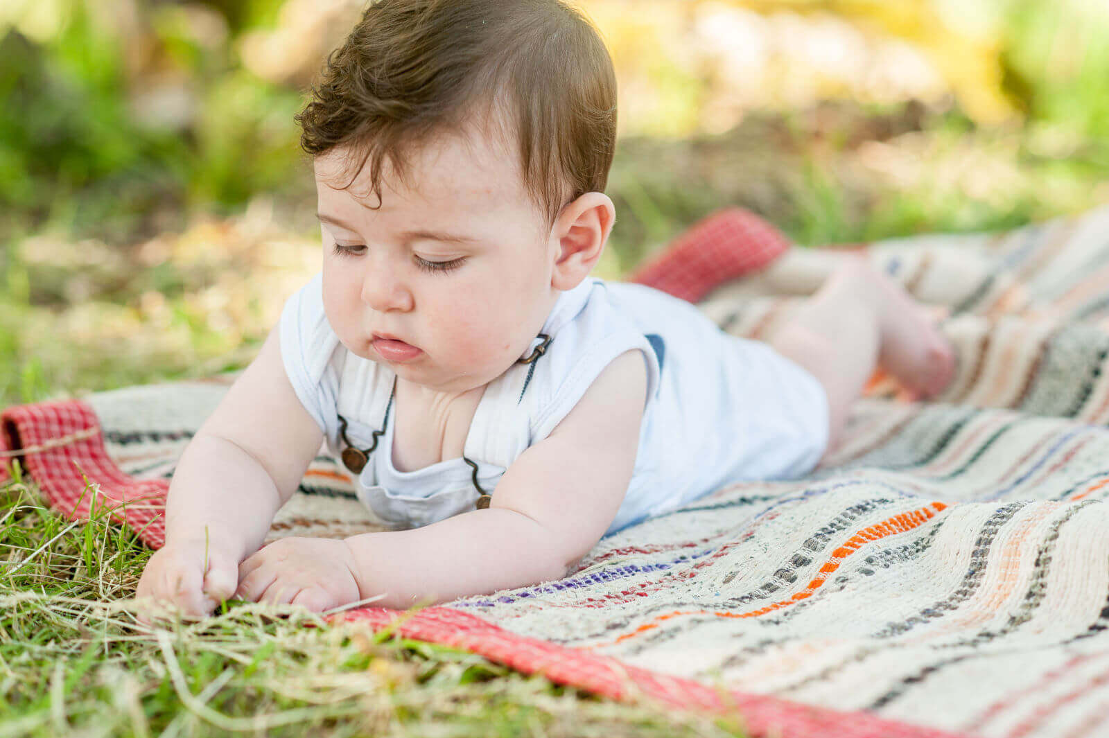 Baby liegt auf einer Decke und erkundet das Gras