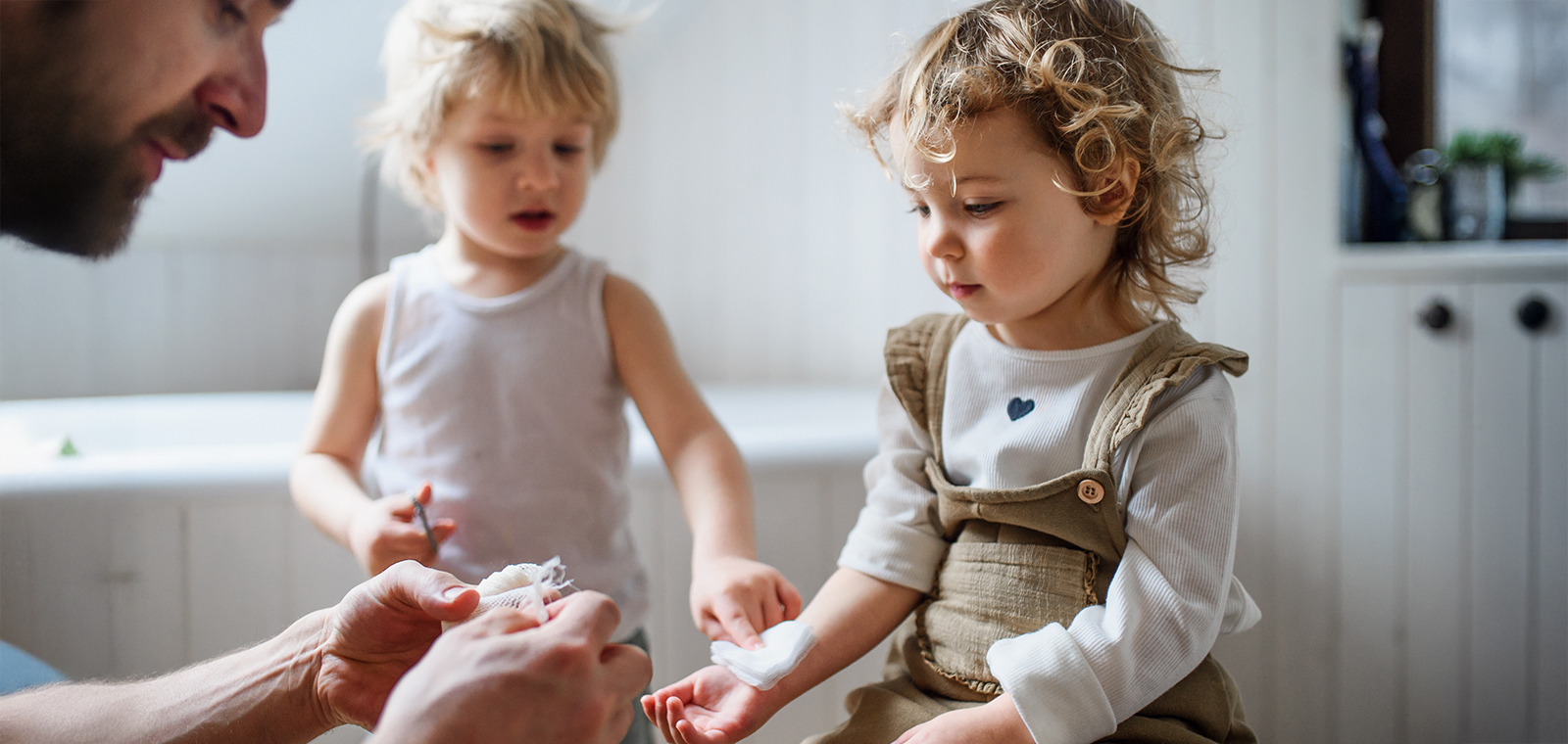 Headerbild Vater mit Kindern beim Verband anlegen